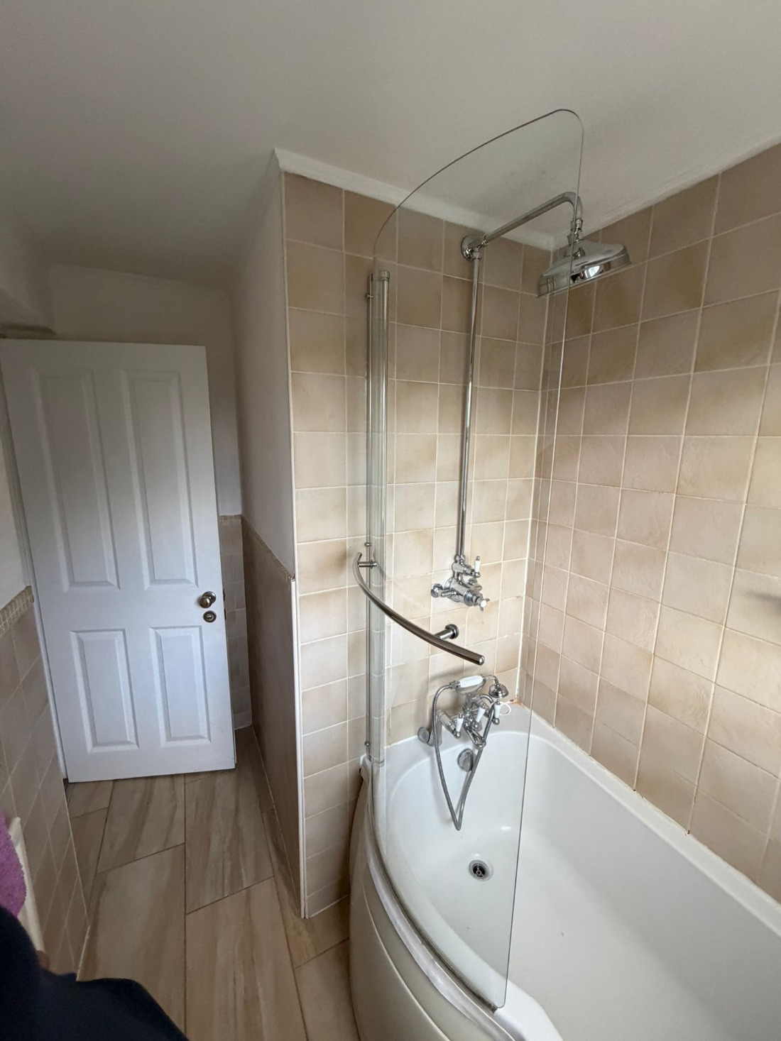 Exposed thermostatic shower with fixed head and curved glass screen over a white bath