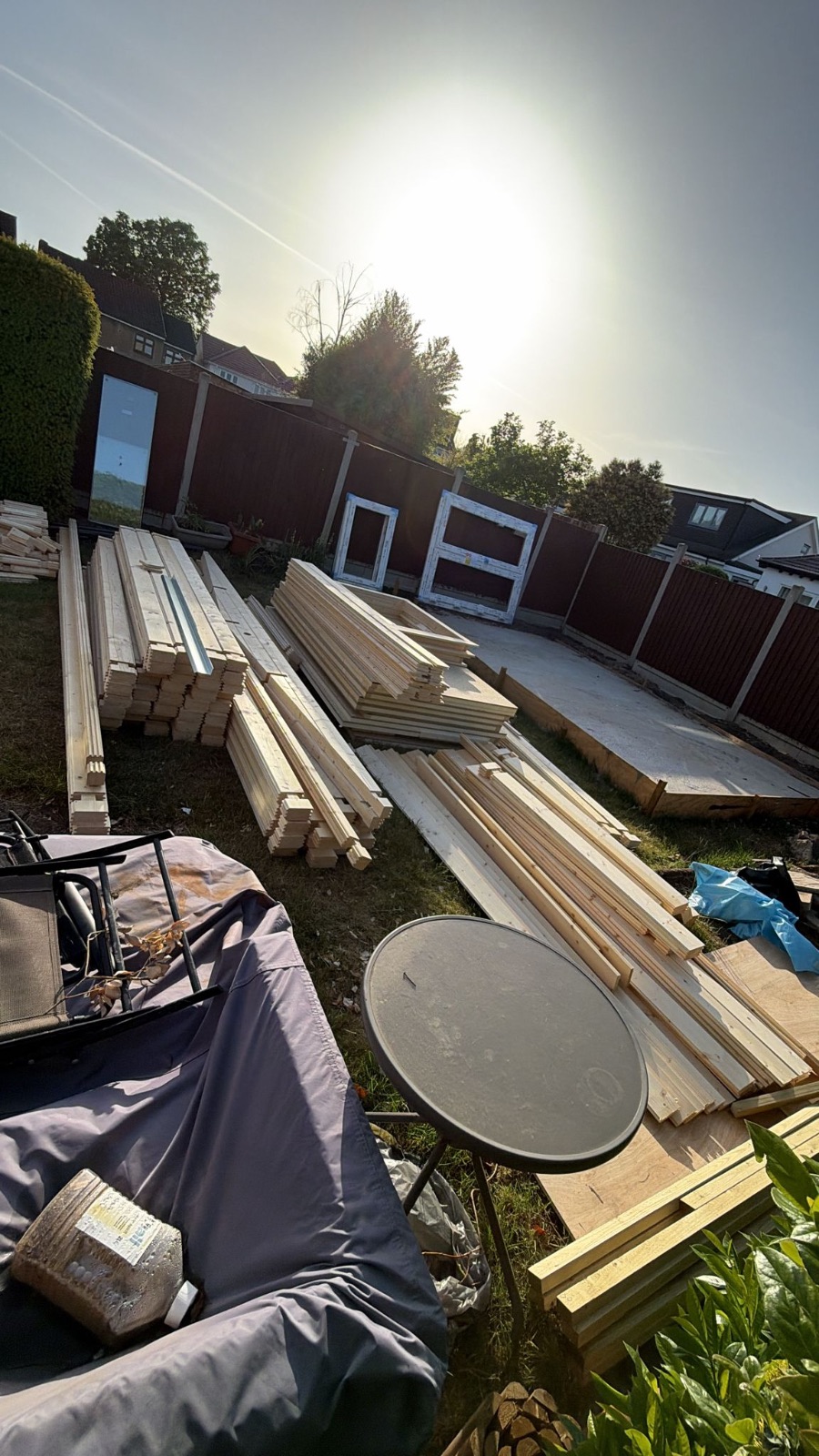Timber wall logs, boards and window frames delivered and stacked beside the concrete base