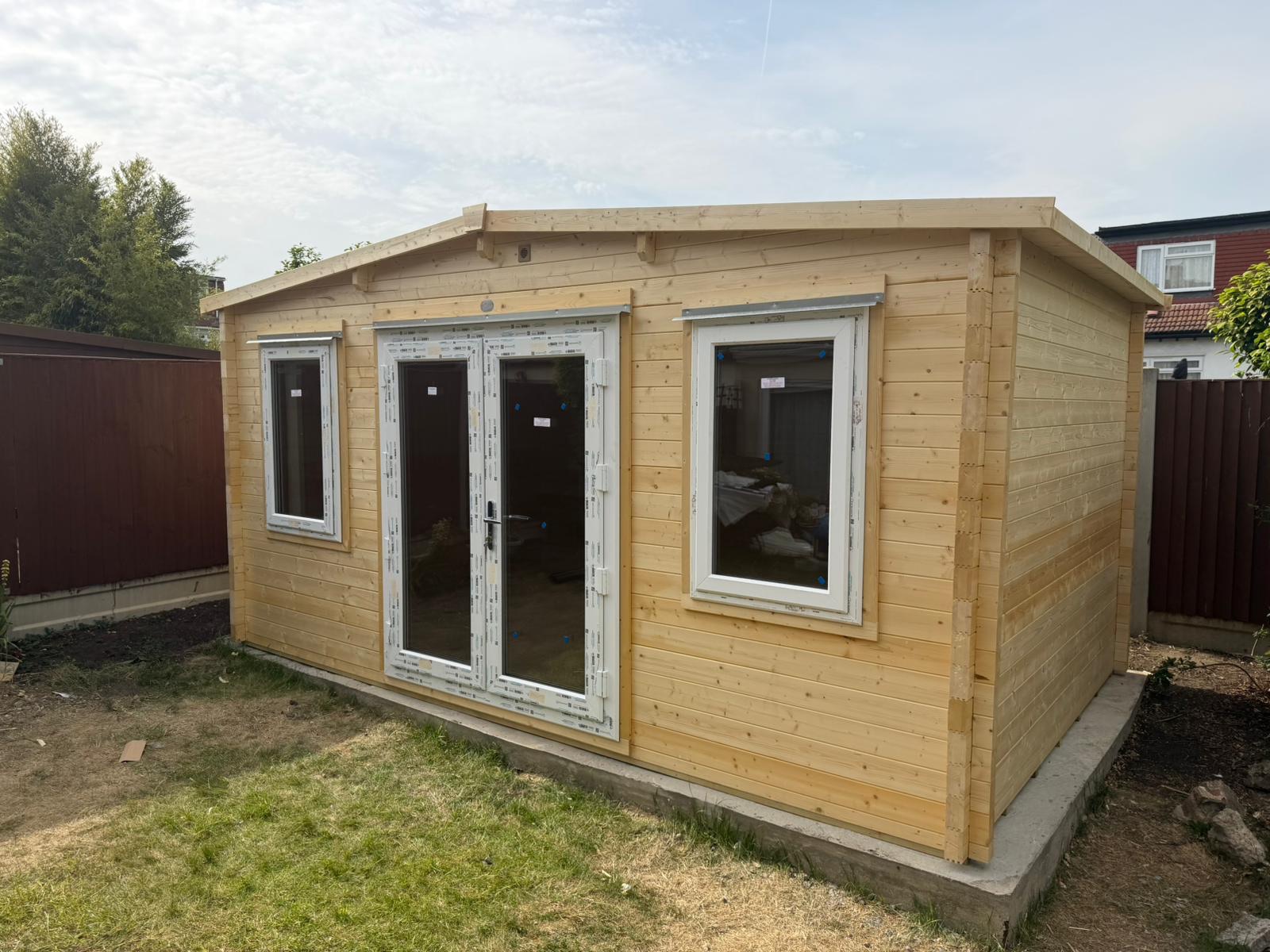 Completed timber garden building with French doors and two uPVC windows on a concrete base